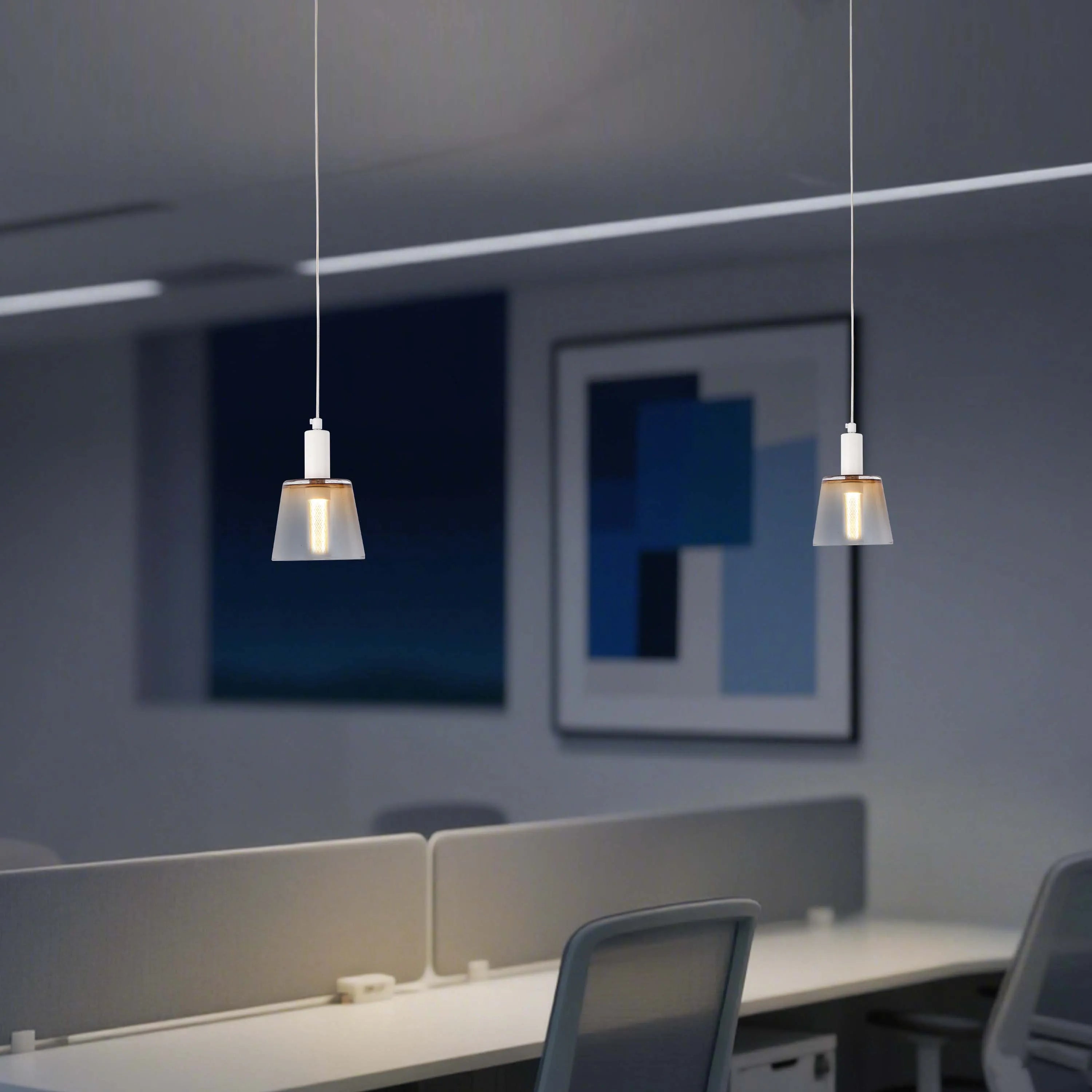 Modern pendant lights hang above desks in a shared office space, creating a bright and stylish working environment.