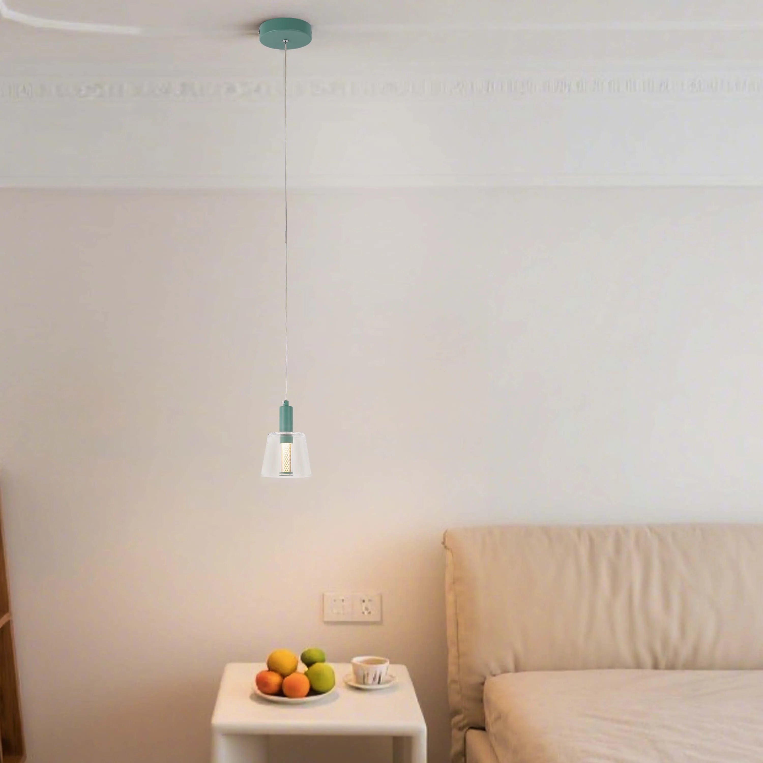 Pendant light with clear glass shade and teal accents, hanging above a bedside table in a bedroom setting.