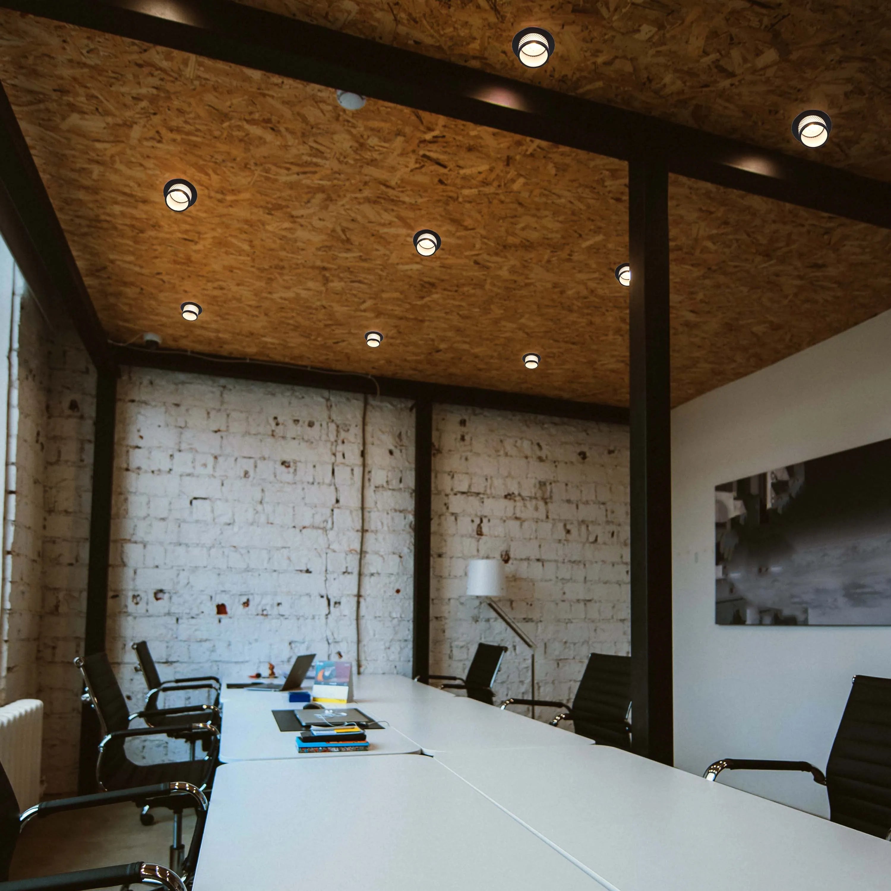 Recessed downlights illuminate a modern office space. Their sleek design blends seamlessly with the OSB ceiling for a minimalist aesthetic.
