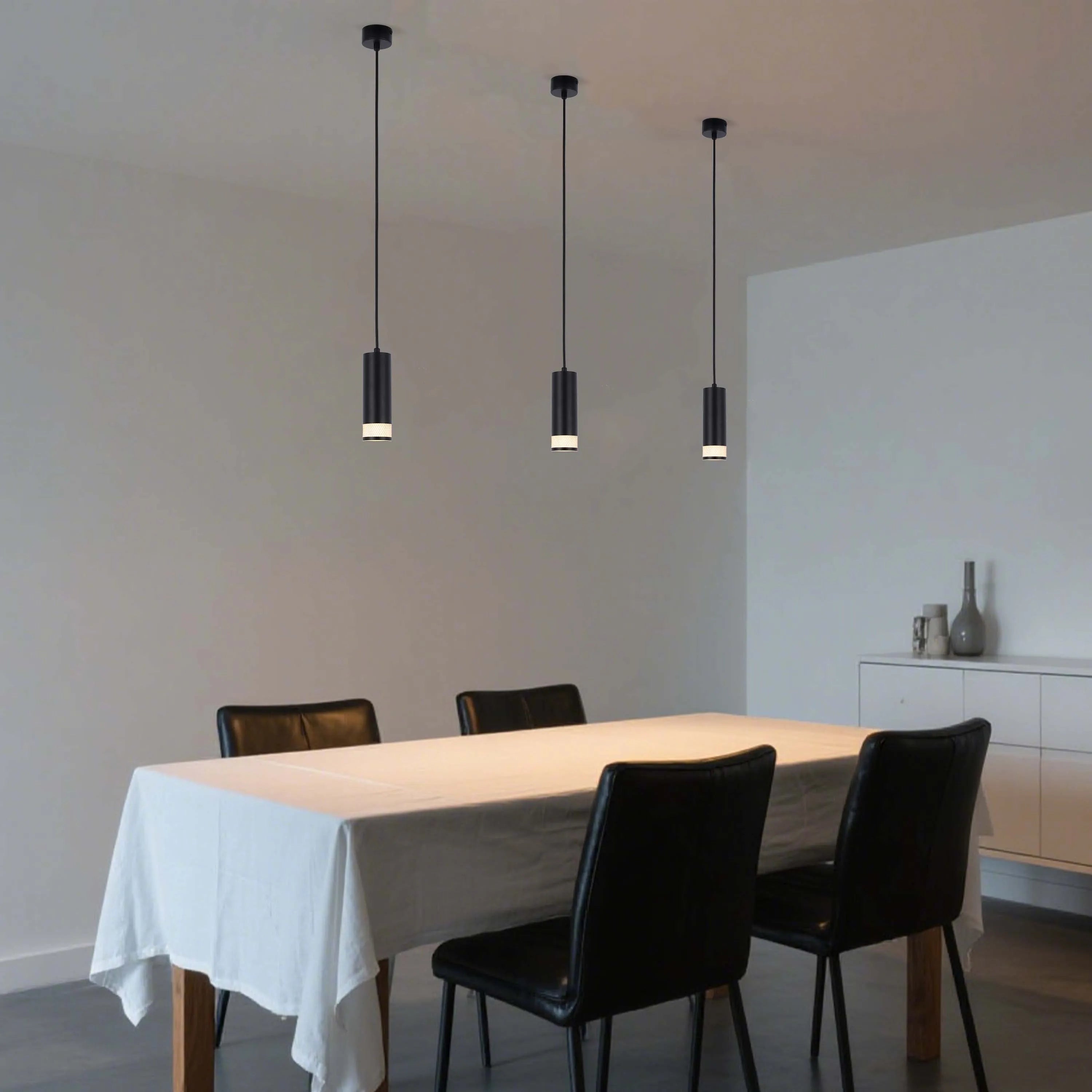 Three modern black pendant lights hang above a dining table, emitting a warm glow. A minimalist and stylish lighting solution.