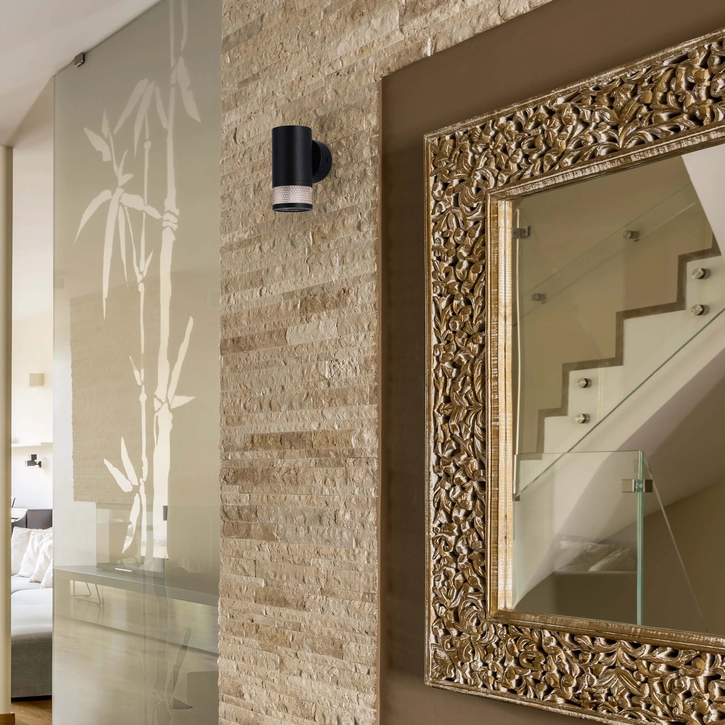 Contemporary black wall light with a patterned mesh base, mounted on a stone feature wall for stylish illumination.