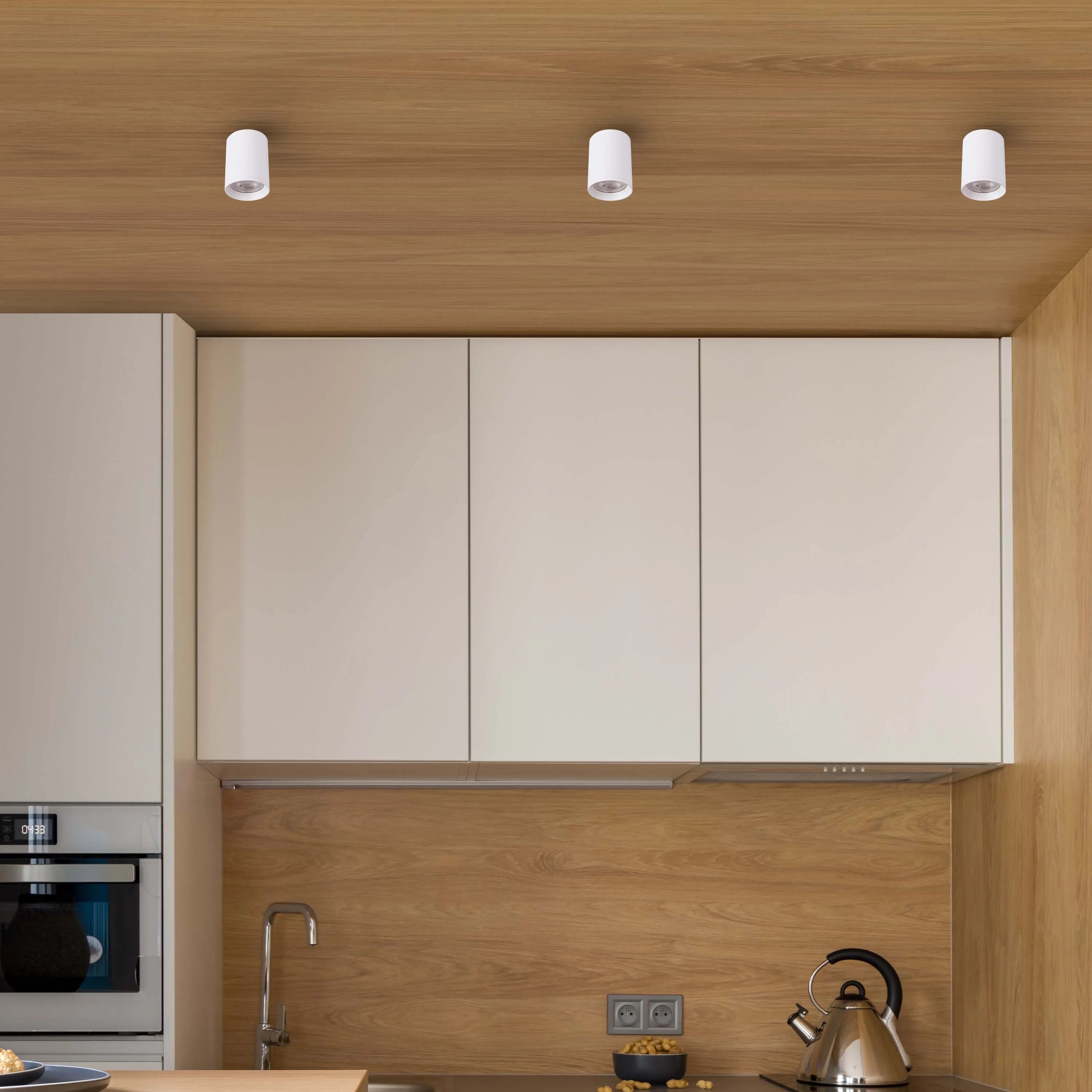 Three white, cylindrical spotlights are recessed into the light-wooden panelled ceiling in this modern kitchen.