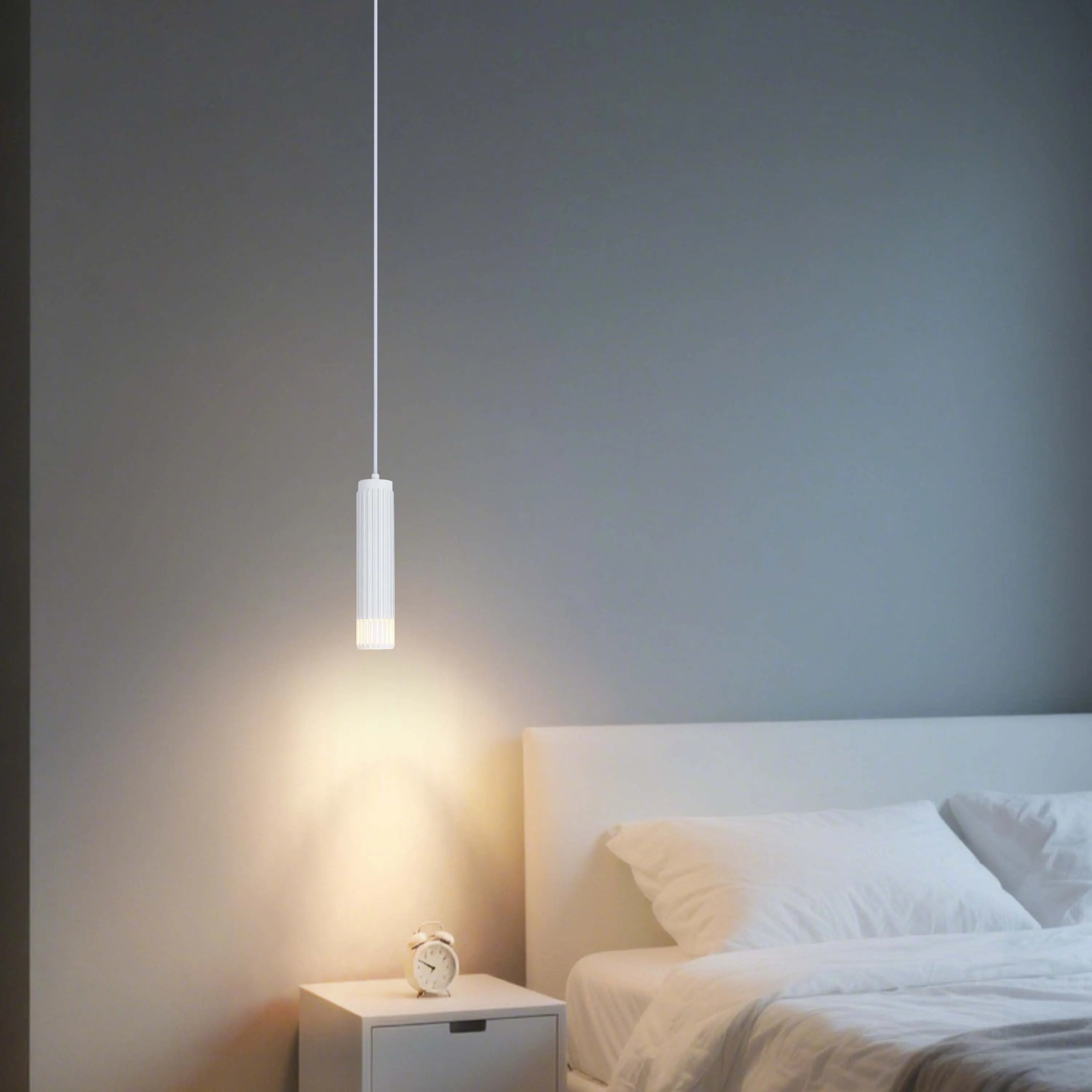 A modern bedroom features a sleek, white pendant light illuminating a bedside table, casting a warm glow in the room.