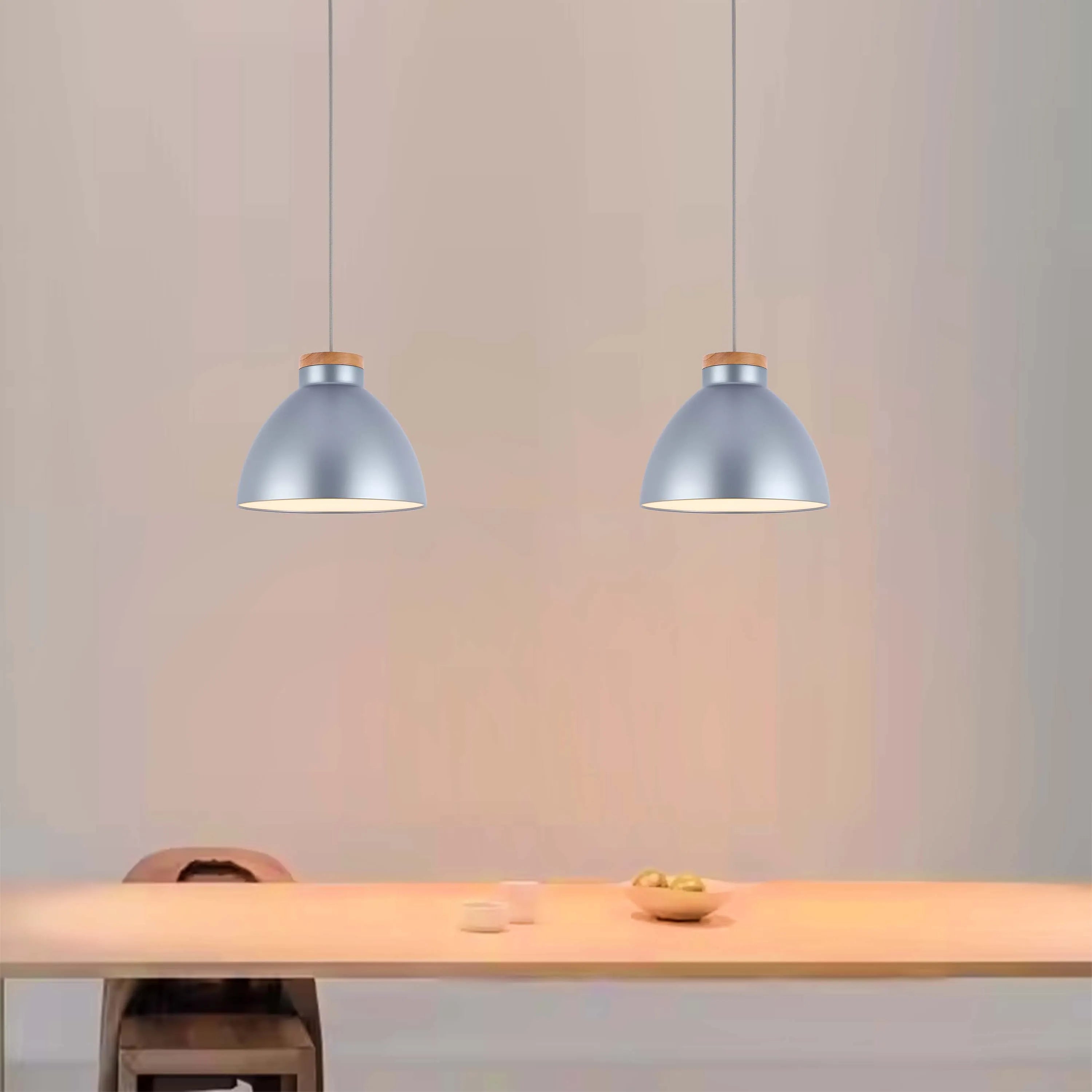 Two dome-shaped, silver pendant lights with wood tops illuminate a light wooden table. Modern, minimalist lighting design.