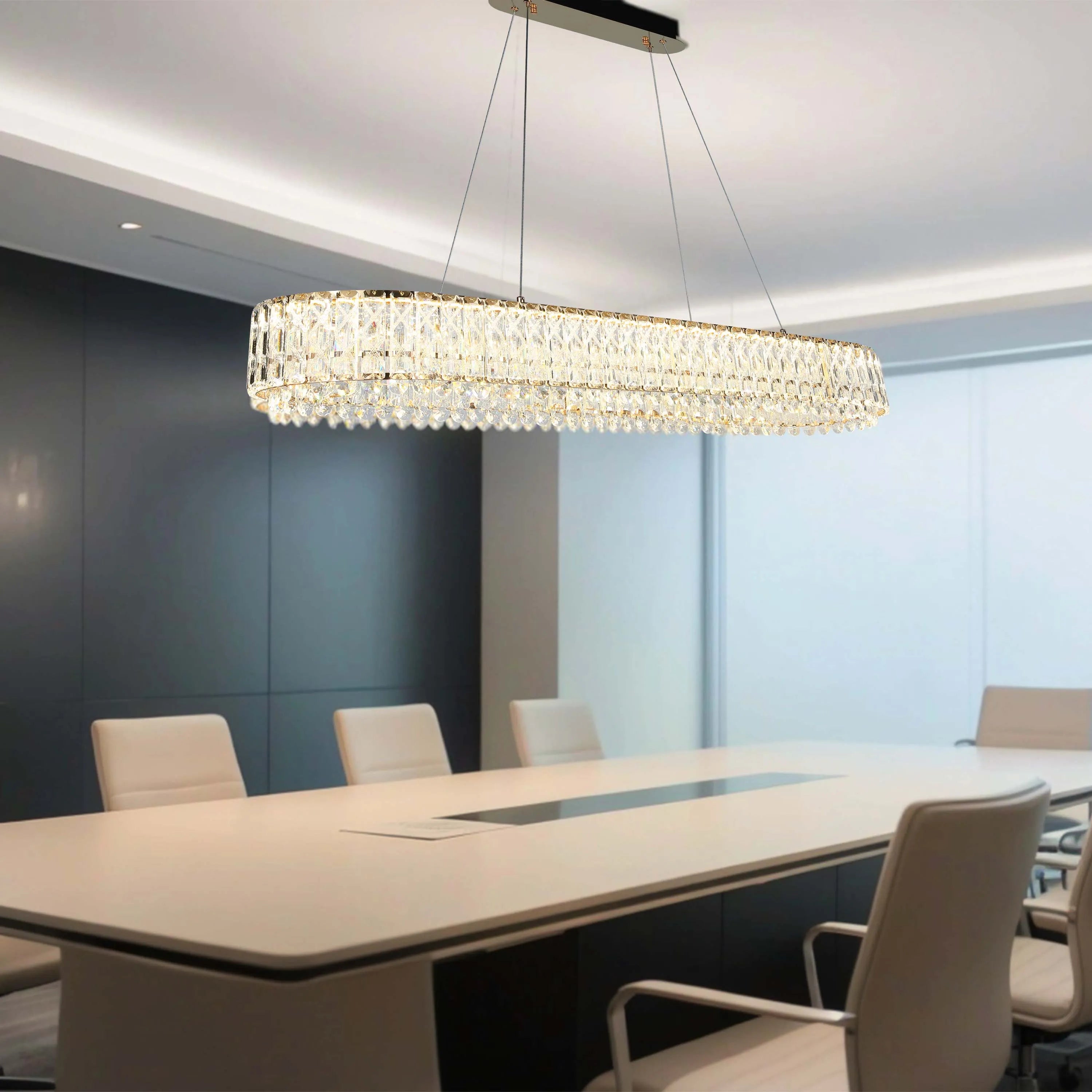 A modern rectangular crystal chandelier hangs above a conference table in an office. It features a gold finish and sparkling crystals.