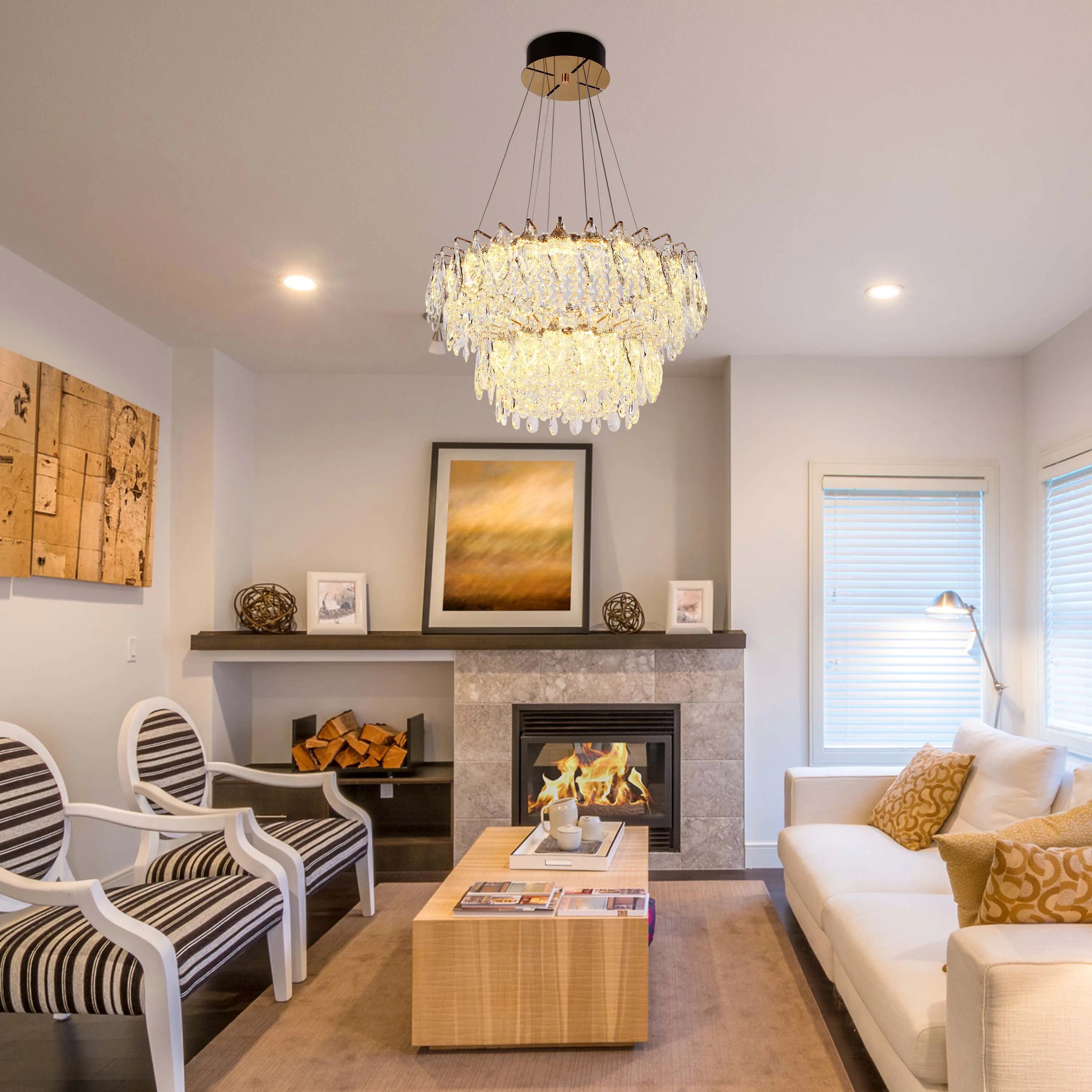 A stylish chandelier hangs above a cosy living room with recessed ceiling lights. Fireplace and lamp provide ambient light.