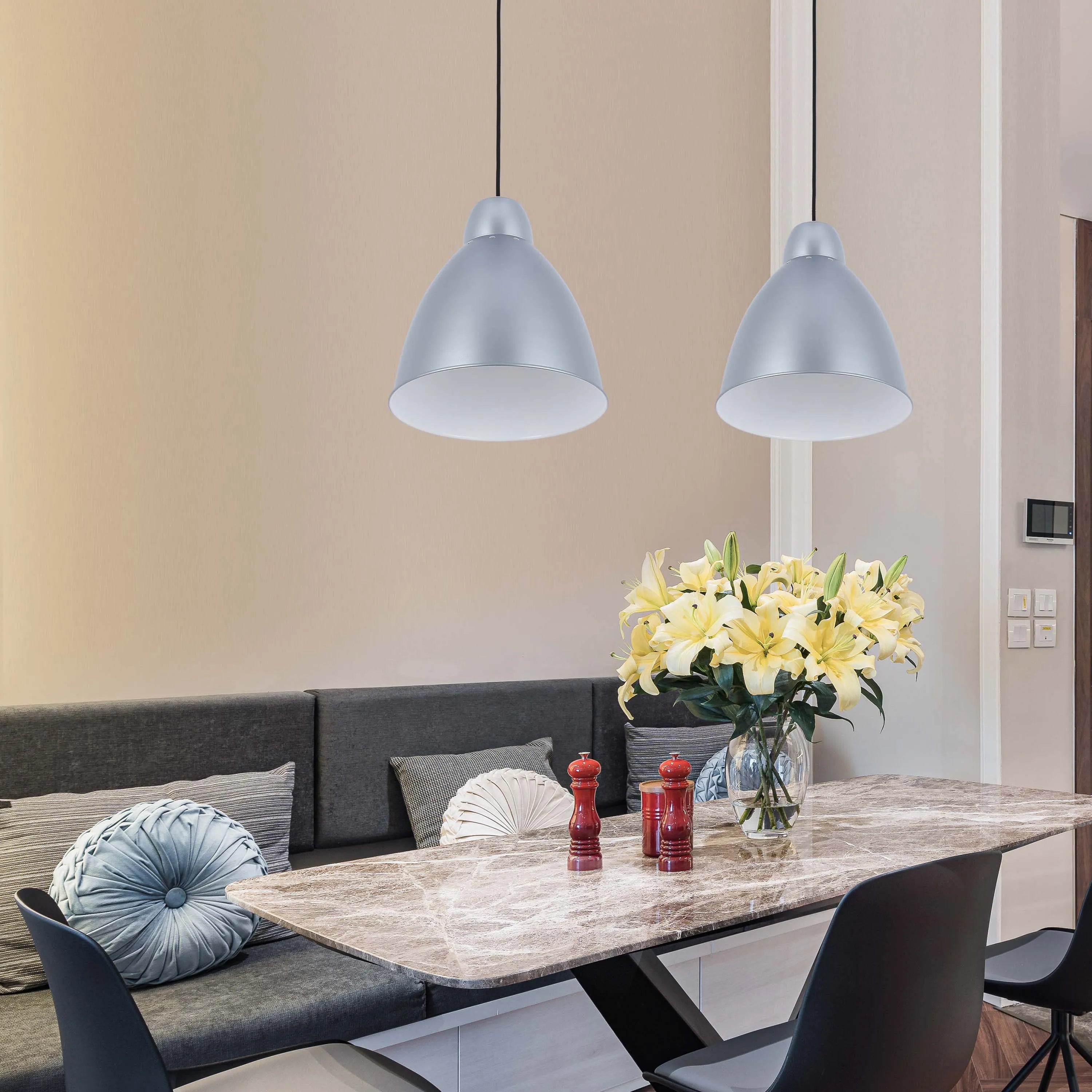 Two silver pendant lights illuminate a dining table with flowers and stylish chairs, creating a modern and inviting atmosphere.