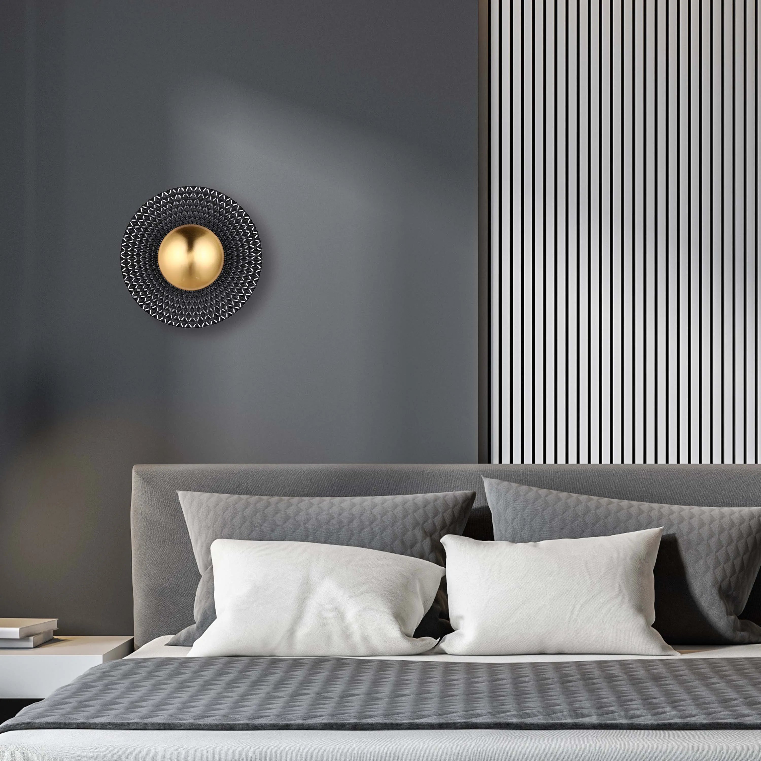 A modern wall light features a central gold sphere surrounded by a geometric, textured disc, adding a touch of contemporary elegance.