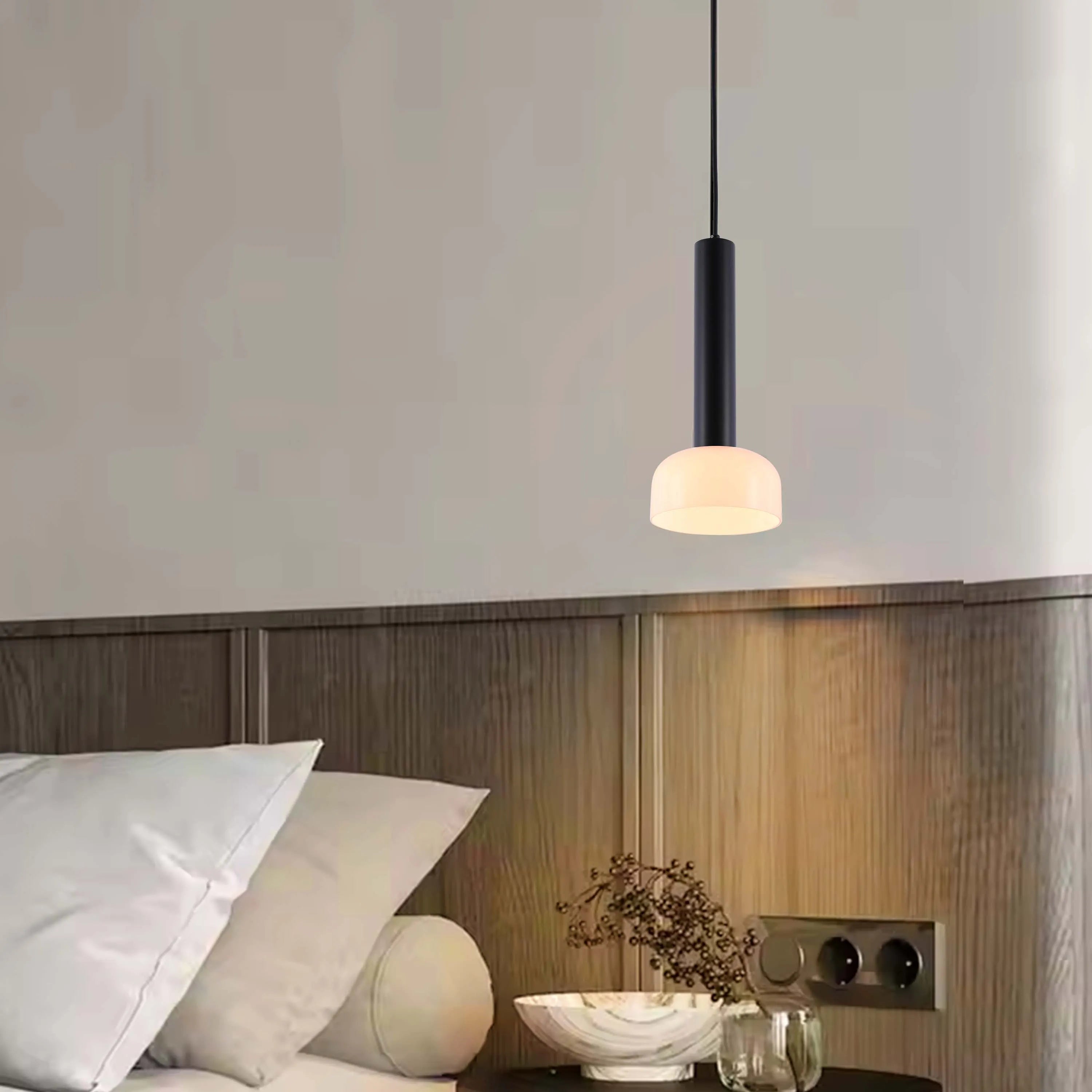 A modern black and white pendant light hangs above a bedside table, creating a cosy, ambient glow.