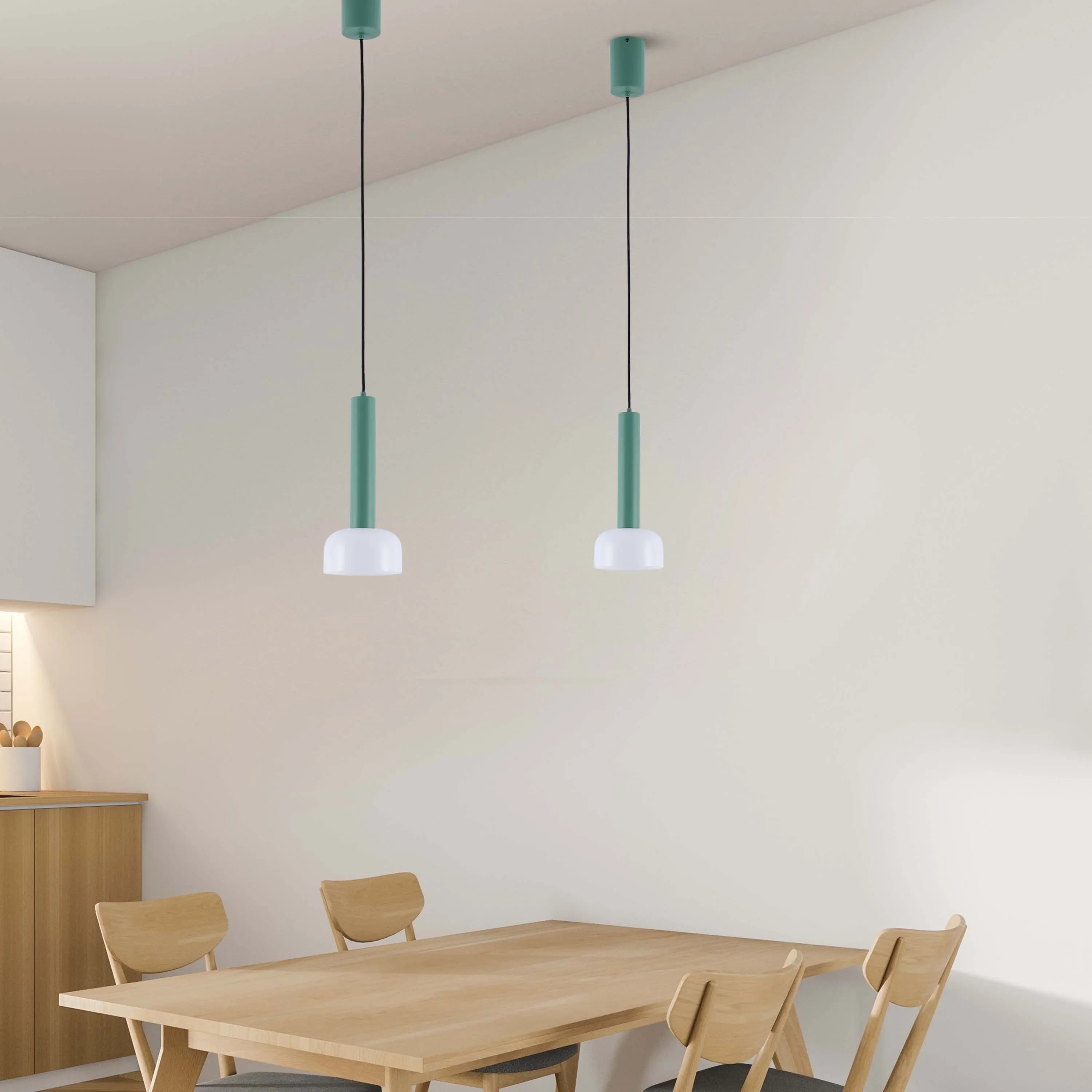 Two modern pendant lights with a green cylinder and white shade hang above a light wood dining table with matching chairs.