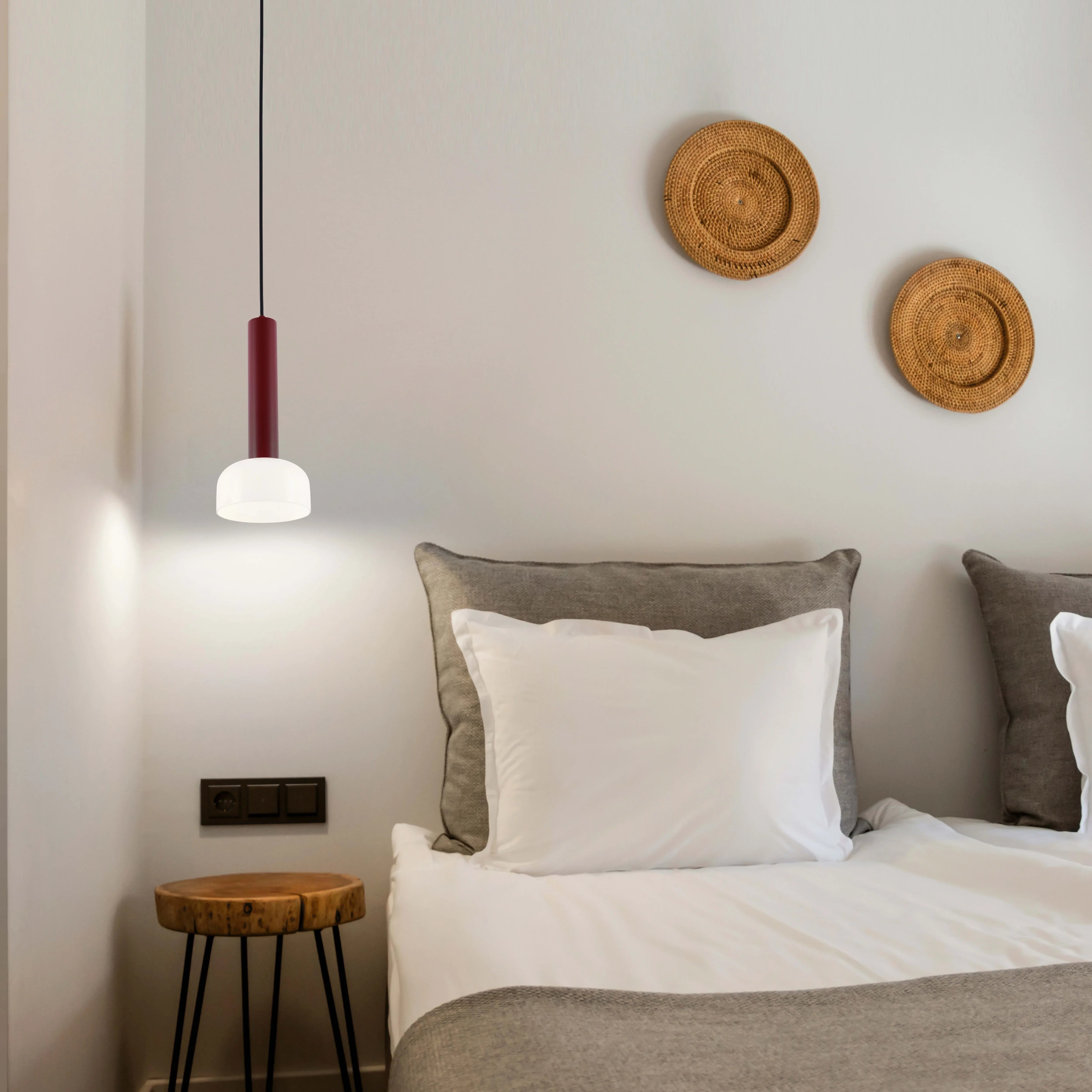 Stylish hanging lamp with a red upper section and a round white shade, illuminating a bedside table in a modern bedroom.