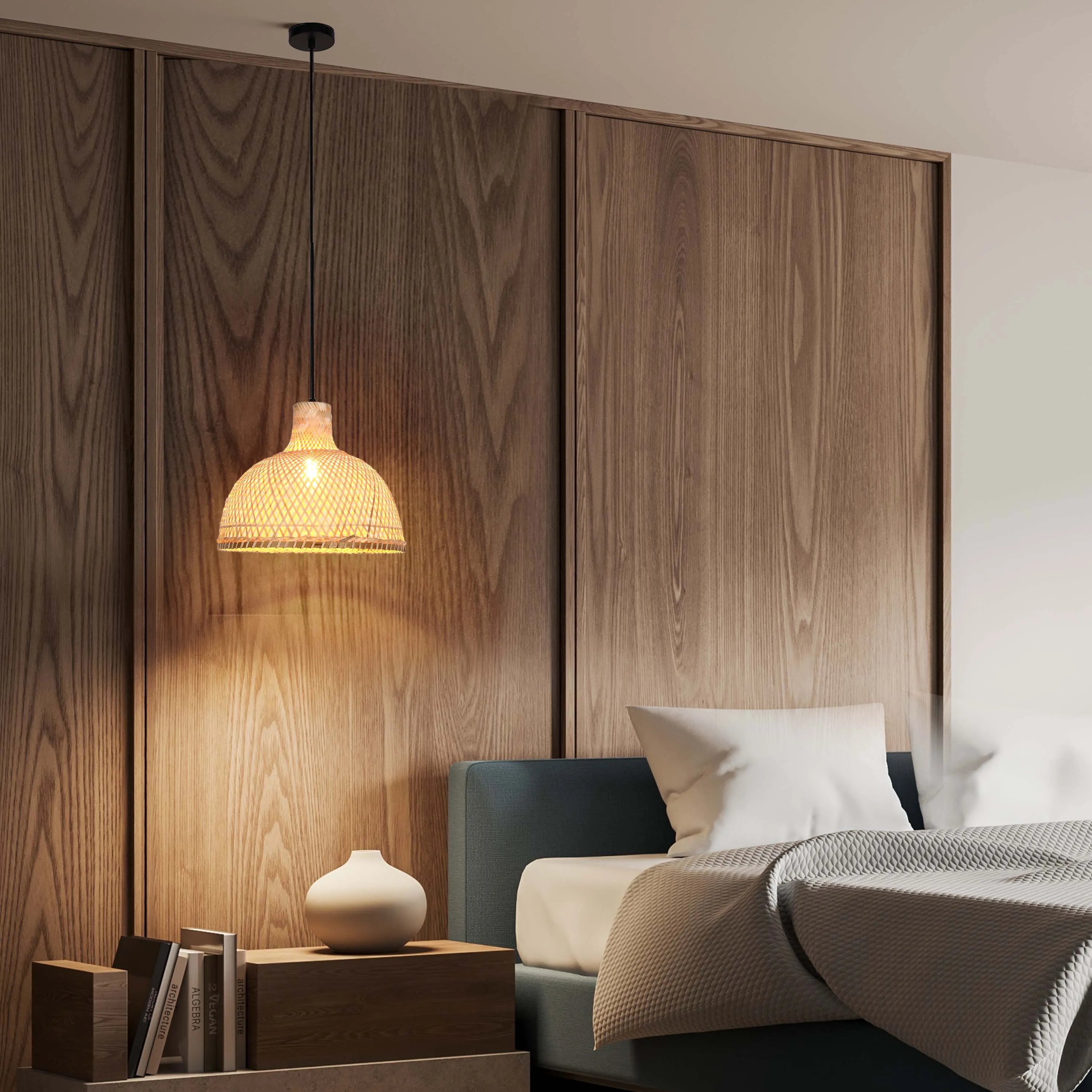 A rattan pendant light with a black cable hangs over a bedside table with a vase and books in a modern bedroom setting.