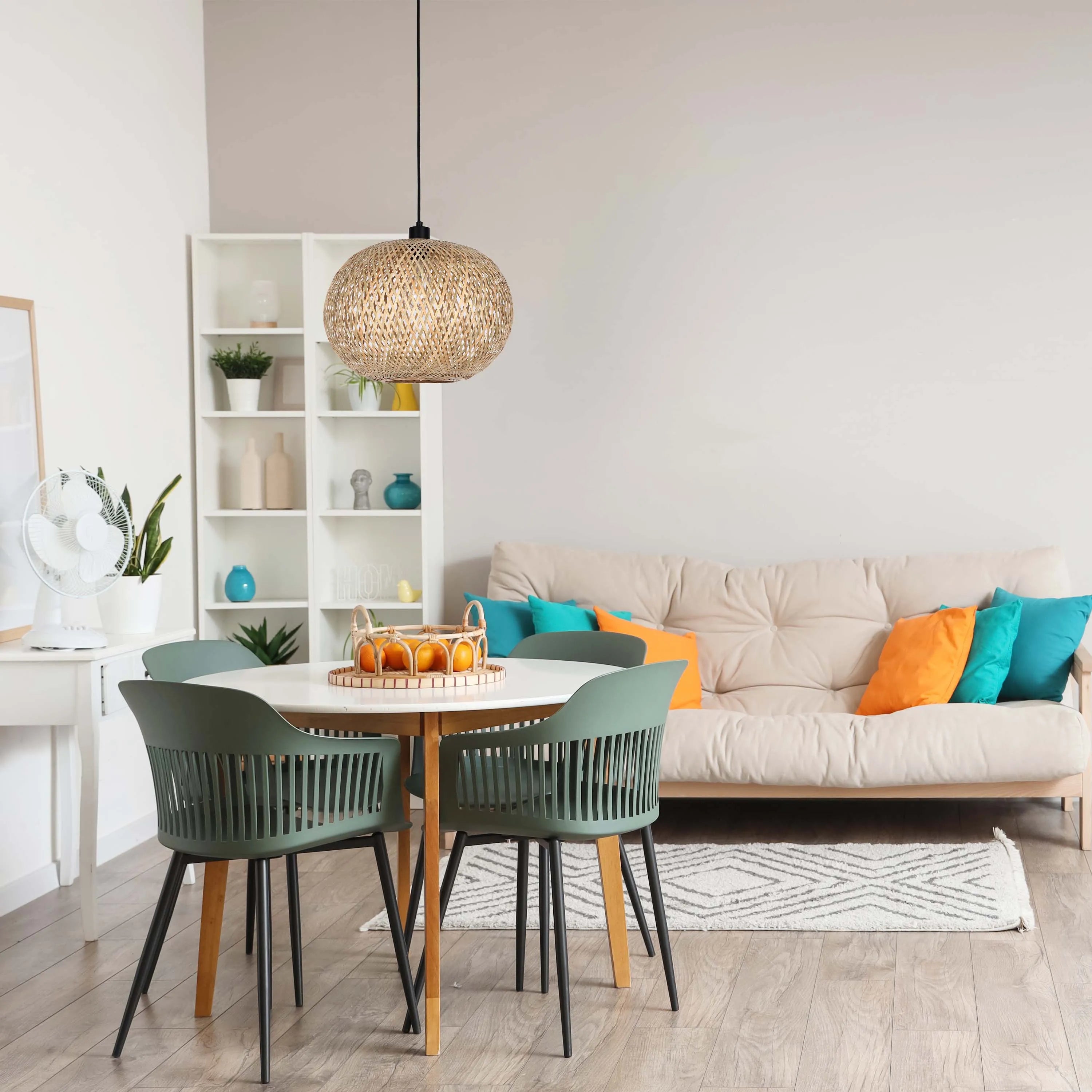 A woven pendant light hangs above a round dining table with modern green chairs in a bright, minimalist dining area.