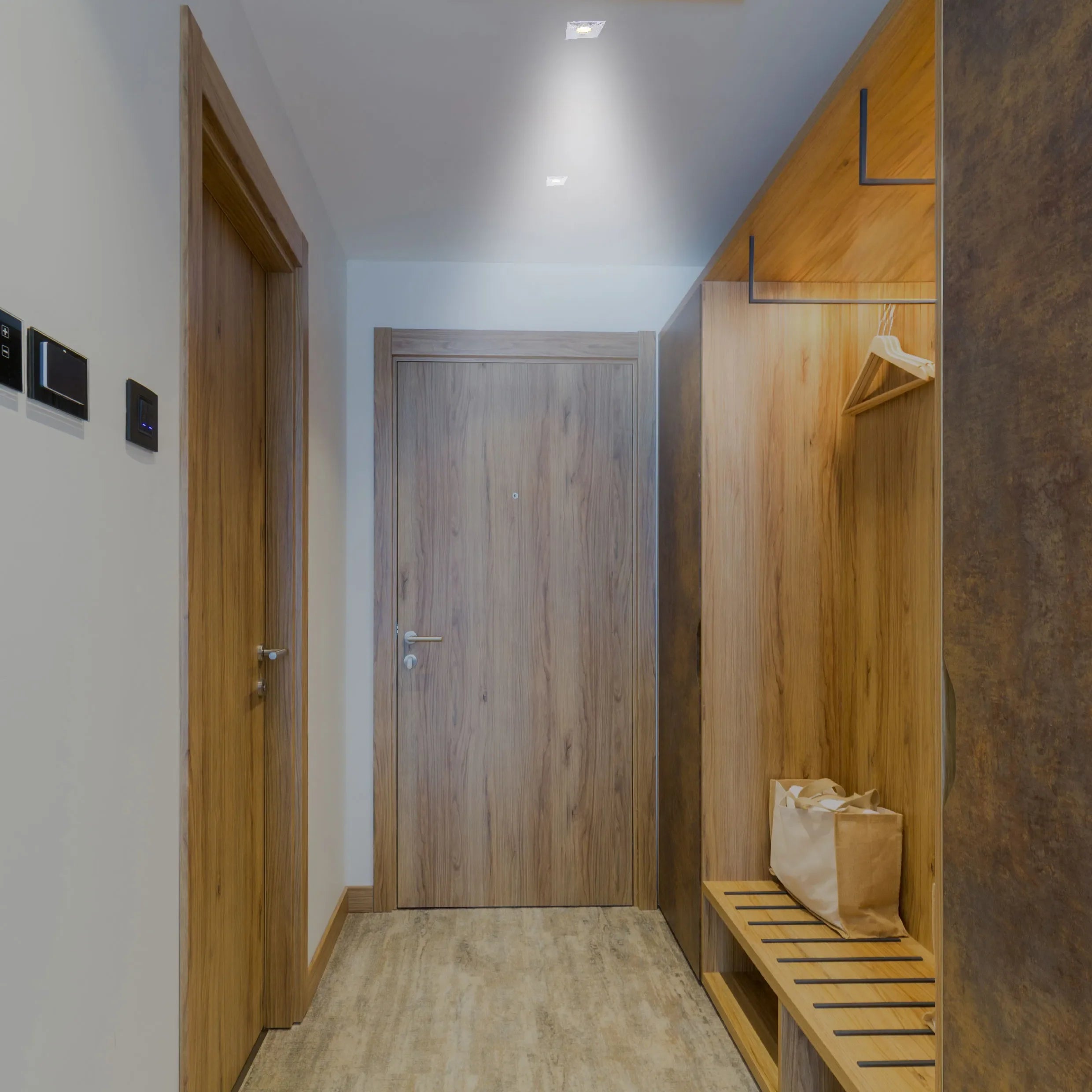 Recessed downlights provide a wash of light, illuminating the modern hallway with fitted wardrobe and light wood doors.