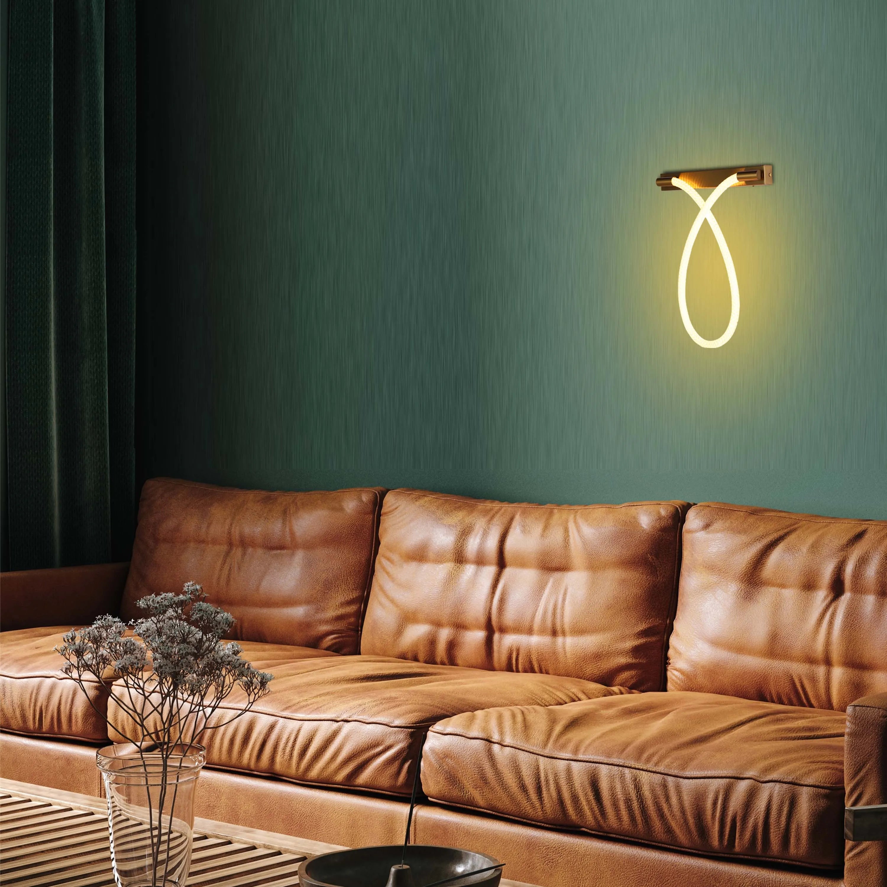 A modern neon wall light in the shape of a loop, casting a warm glow on the green wall above a brown leather sofa.