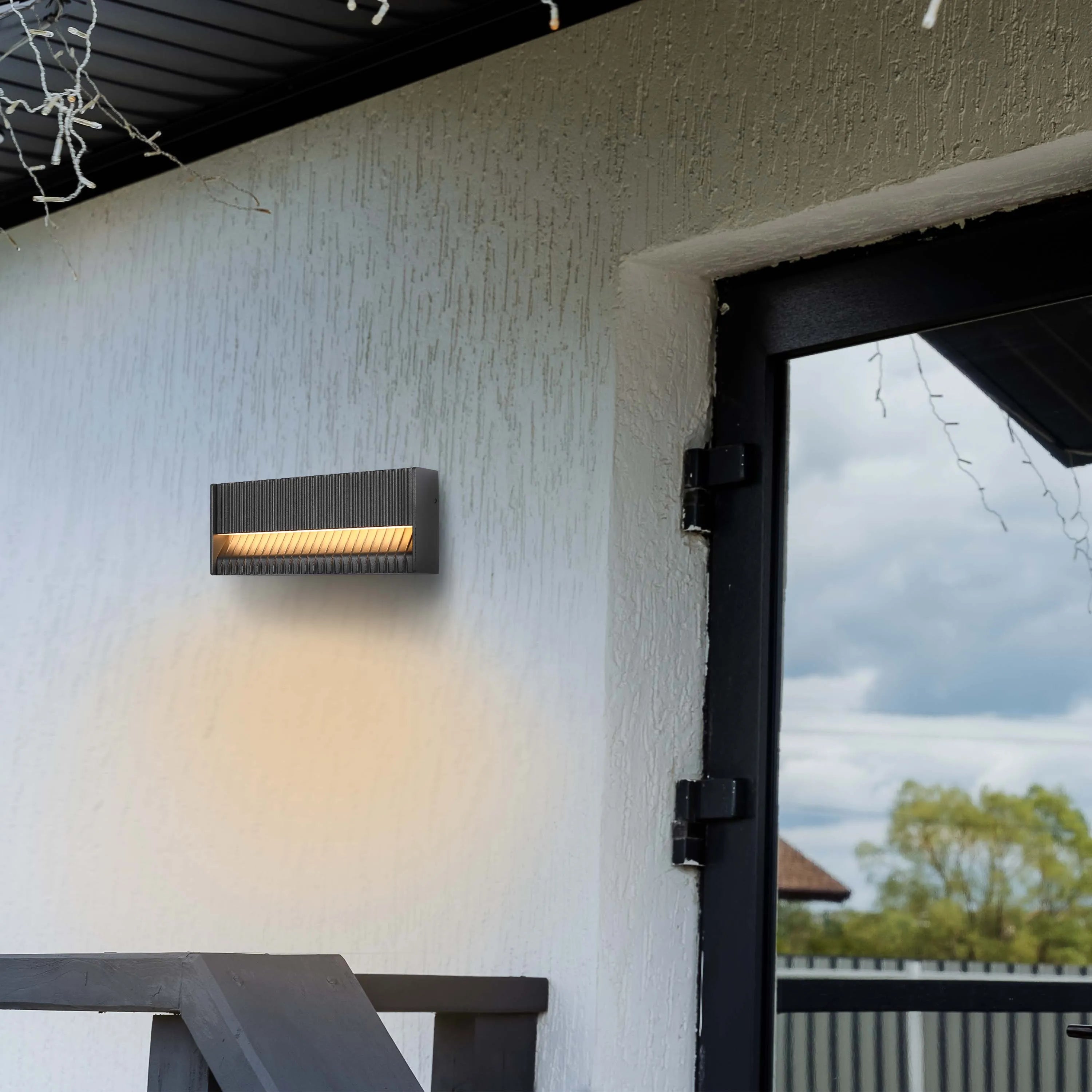 An outdoor wall light, emitting a warm, inviting glow against the textured white facade of a building, creating a welcoming ambience.