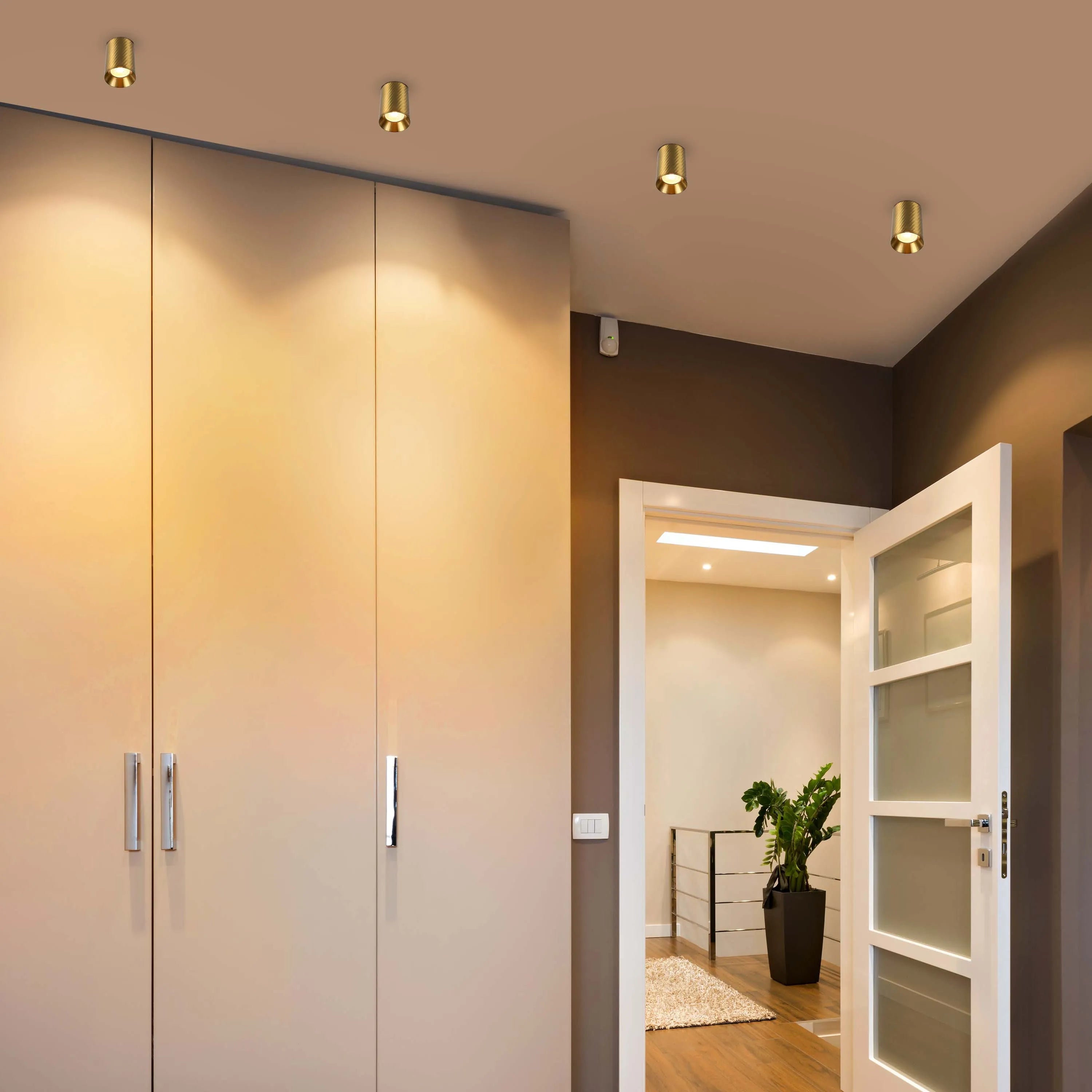 A room lit by four ceiling-mounted, gold-coloured downlights providing focussed illumination.
