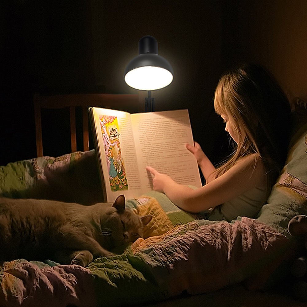 Child reading in bed with a cat and adjustable lamp. Dark wood headboard partially visible.