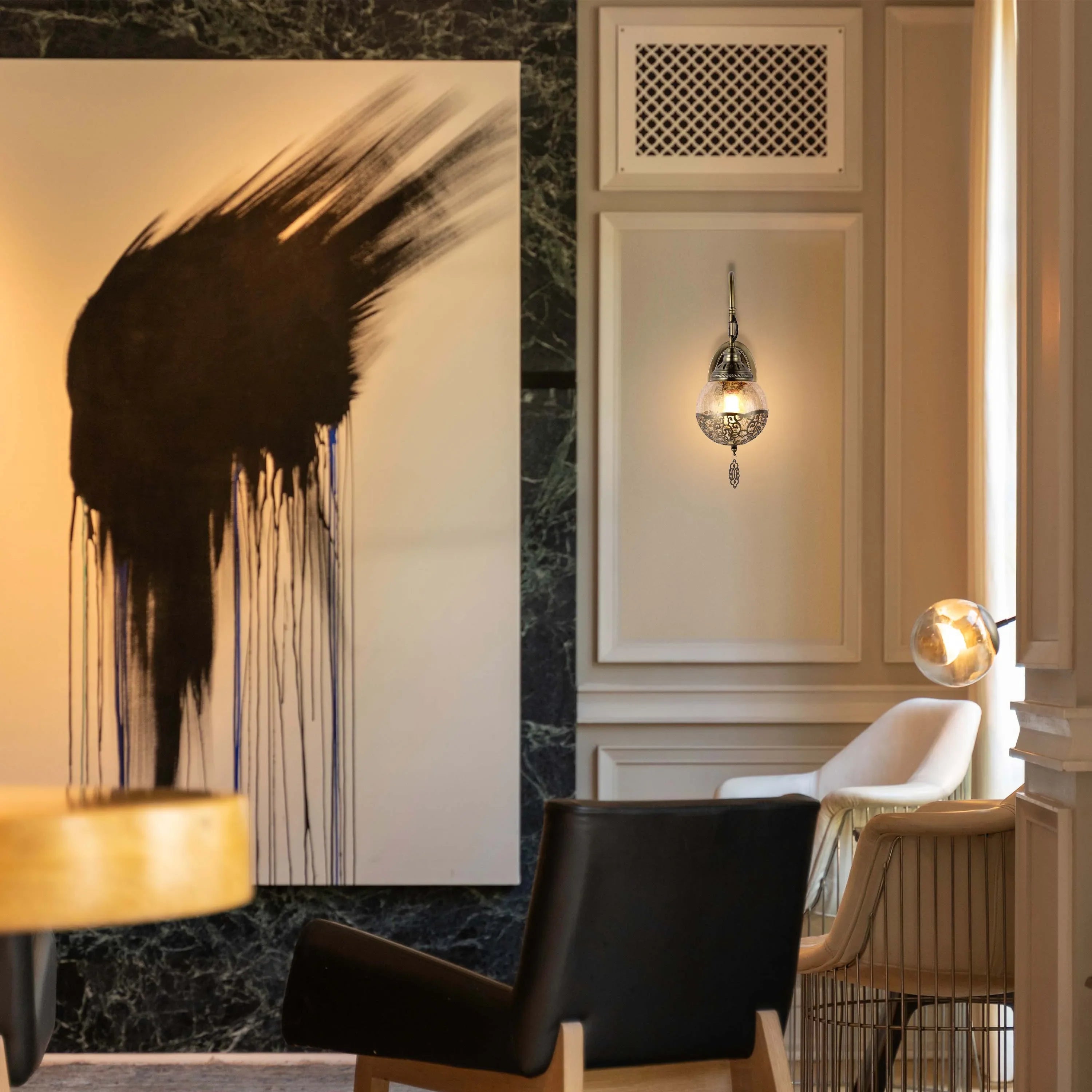 A decorative wall light illuminates the scene, with a spherical design and filigree detailing. A round table lamp is also visible.