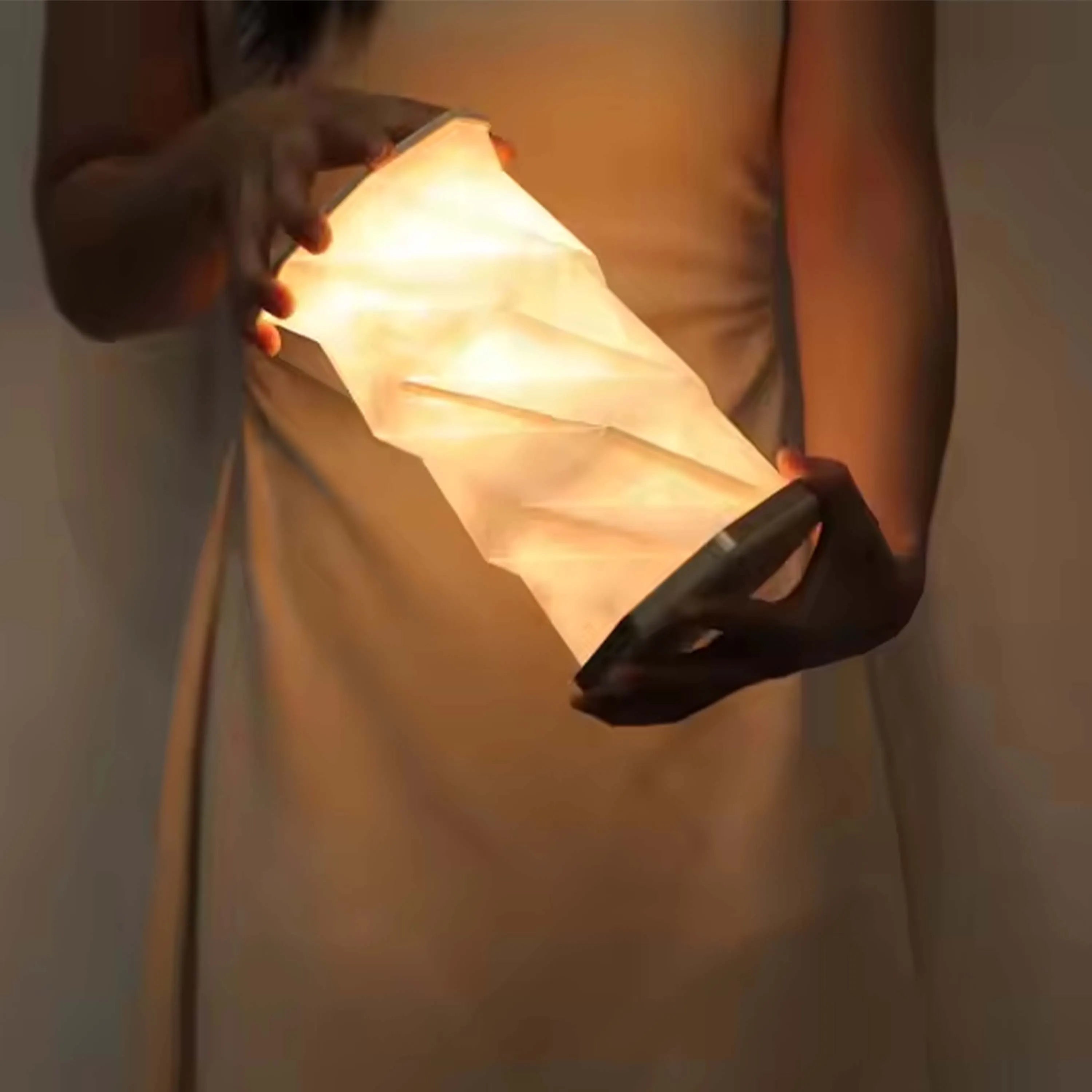 Soft, diffused light glows from a handmade paper lamp. The warm light radiates as it's being held.