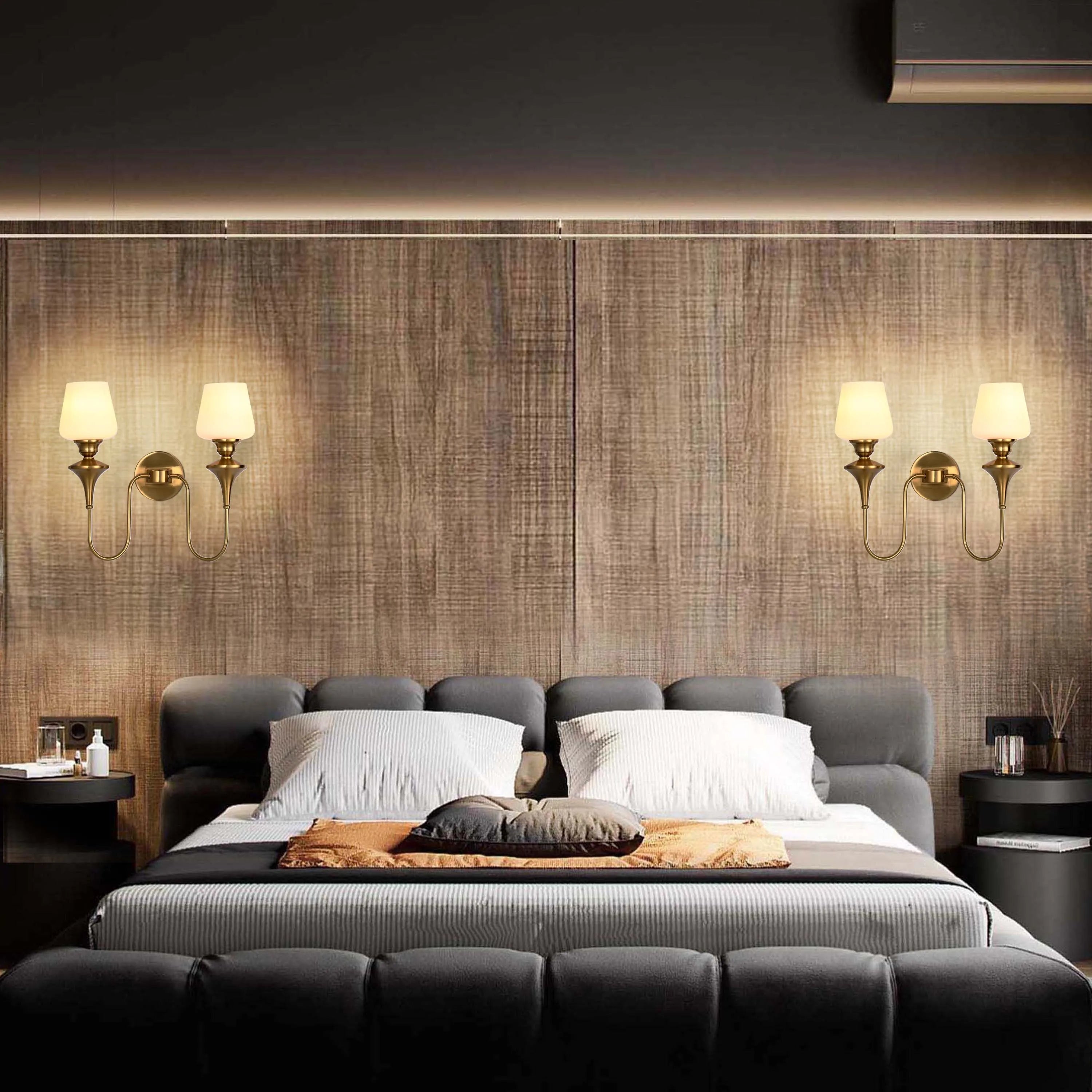 Two wall-mounted sconces with brass fixtures and glass shades illuminate a stylish bedroom, adding a touch of elegance.