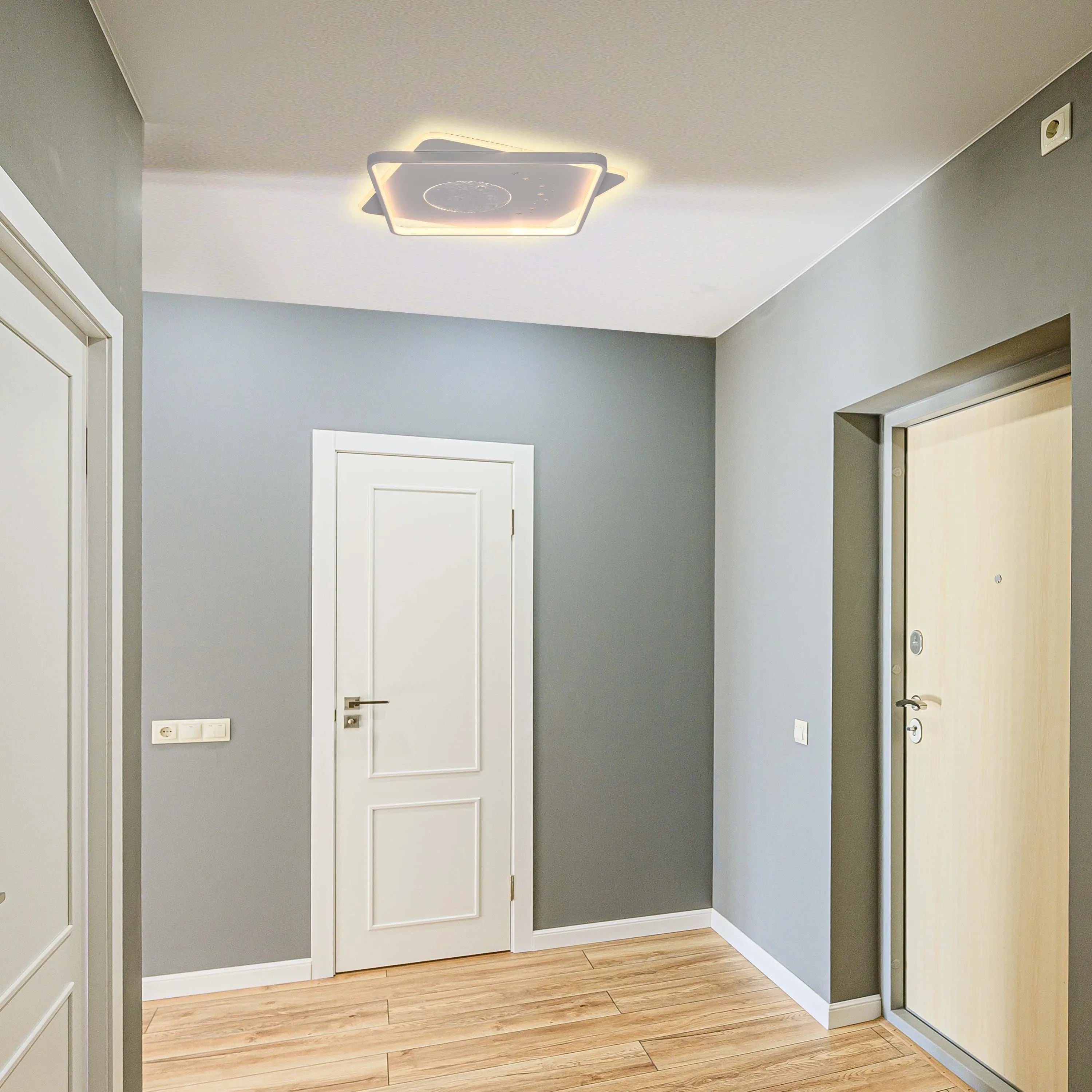 Modern square ceiling light with a celestial design casting a warm glow in a grey hallway.