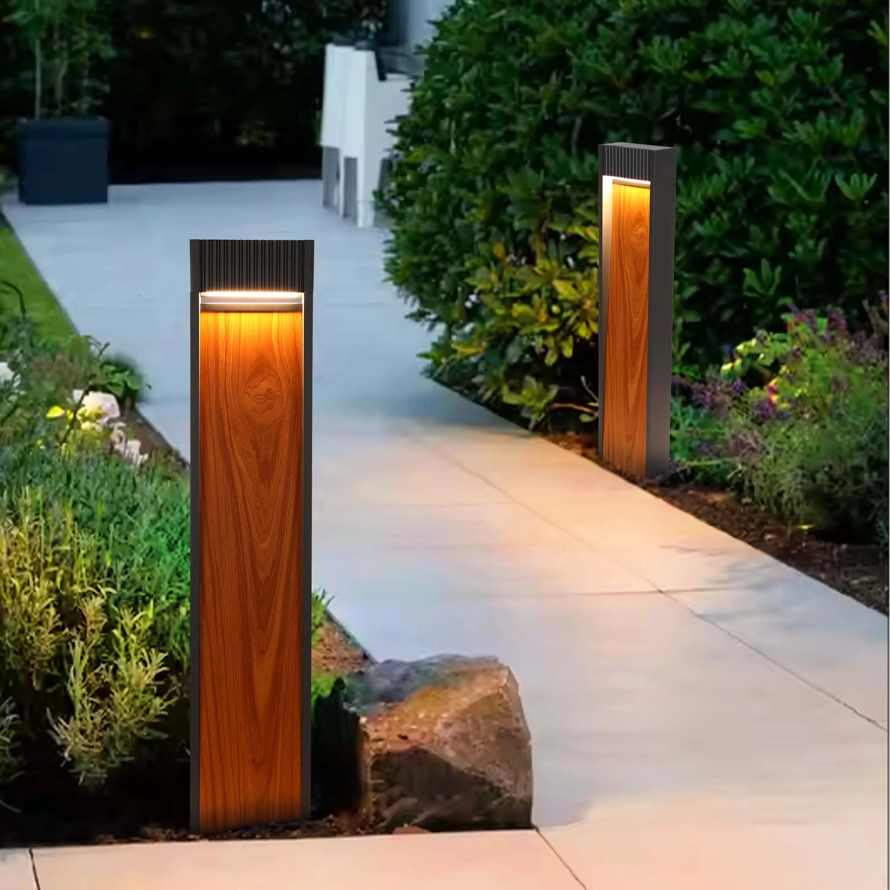 Contemporary outdoor lighting illuminates a pathway. Two modern, wooden style bollard lights brighten a garden path at night.